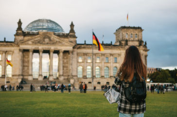A tourist girl with a backpack next to the building called the Reichstag in Berlin in Germany takes pictures. Sightseeing, tourism, travel around Europe
