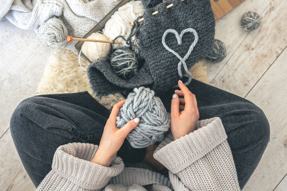 woman-with-gray-threads-knitted-element-sits-floor-top-view